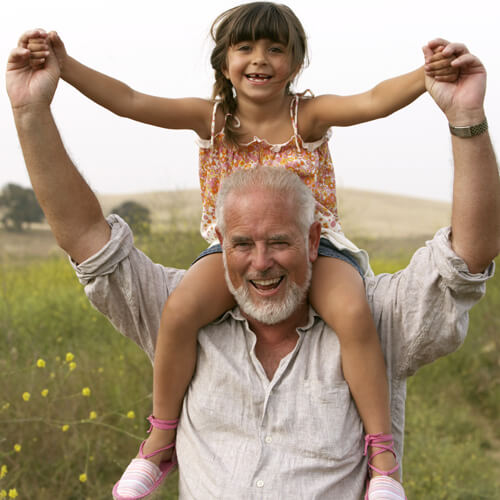 Happy elderly man holds happy child above his shoulders.